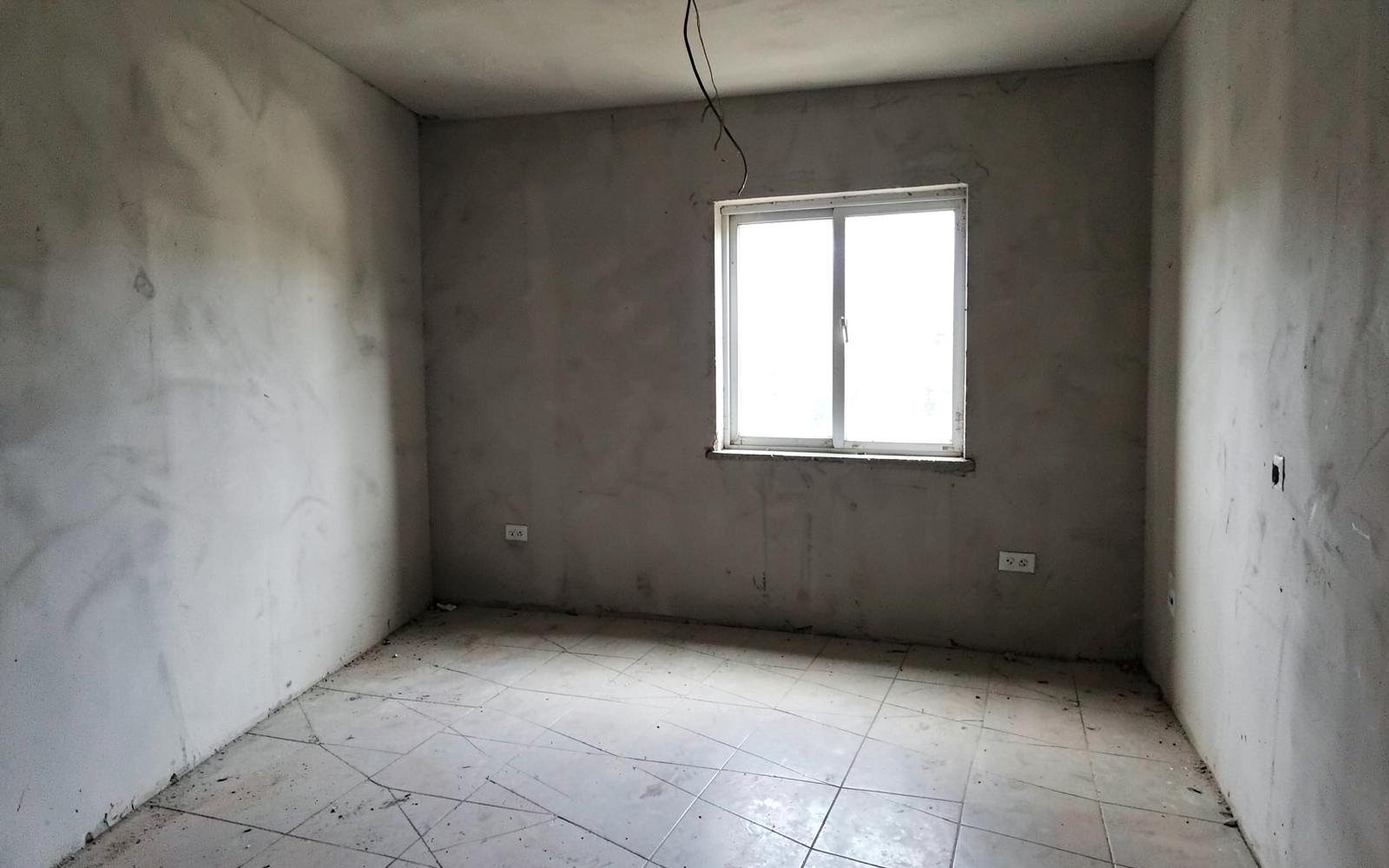 The same room before renovation, bare plaster walls and dusty tile floor